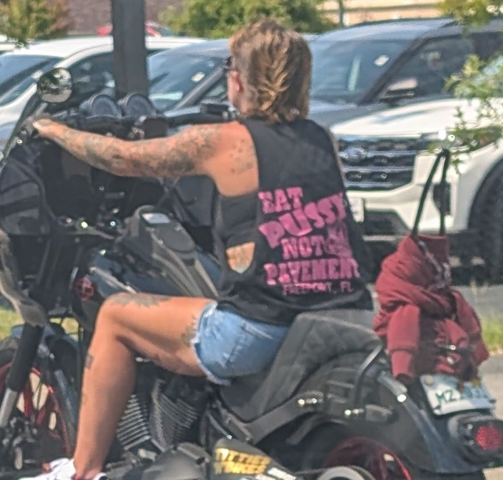 Lady on a motorcycle sporting a shirt that says, EAT PUSSY NOT PAVEMENT