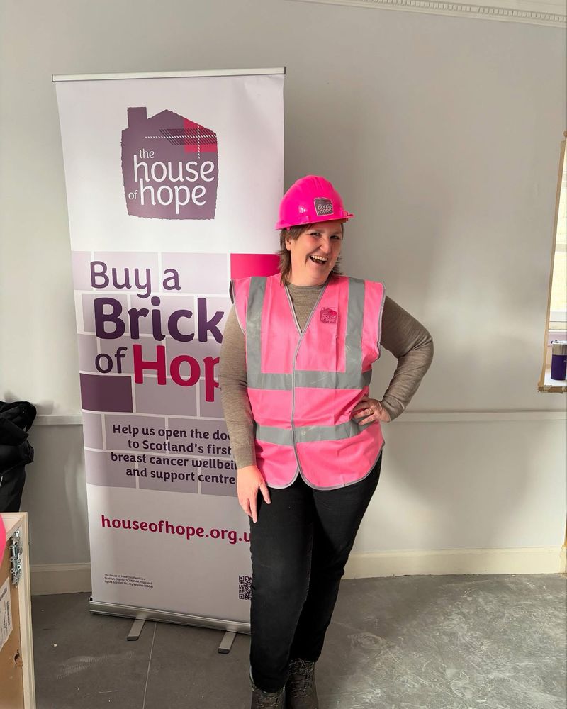 Emma Walker, wearing pink high vis jacket and pink hard hat, in front of House of Hope promotional banner