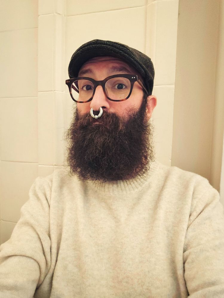 Me sitting against a beige wall in a beige sweater and dark green cap