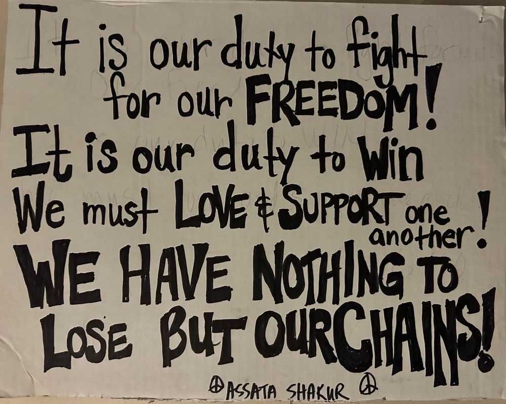Black hand printed sign on white cardboard that reads: It is our duty to fight for our freedom
It is our duty to win
We must love and support one another
We have nothing to lose but our chains

Assata Shakur