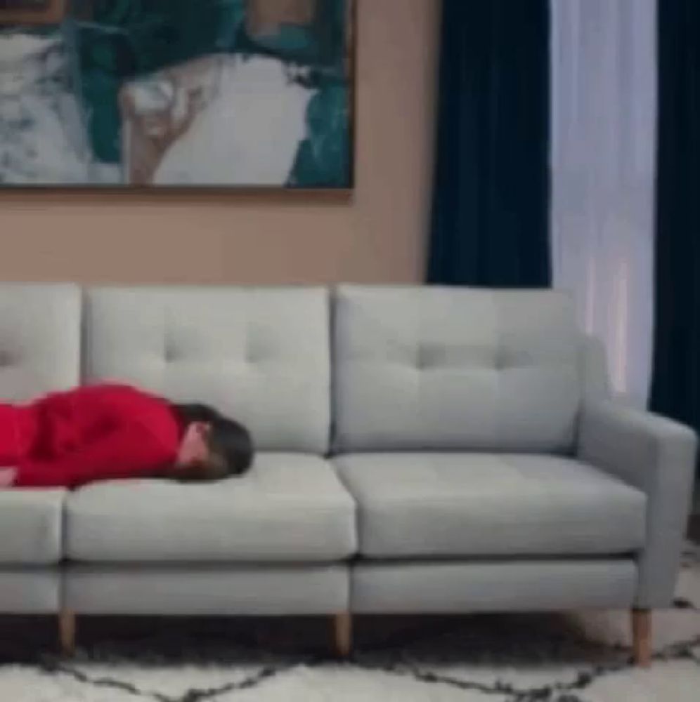 a woman in a red shirt is sleeping on a white couch .