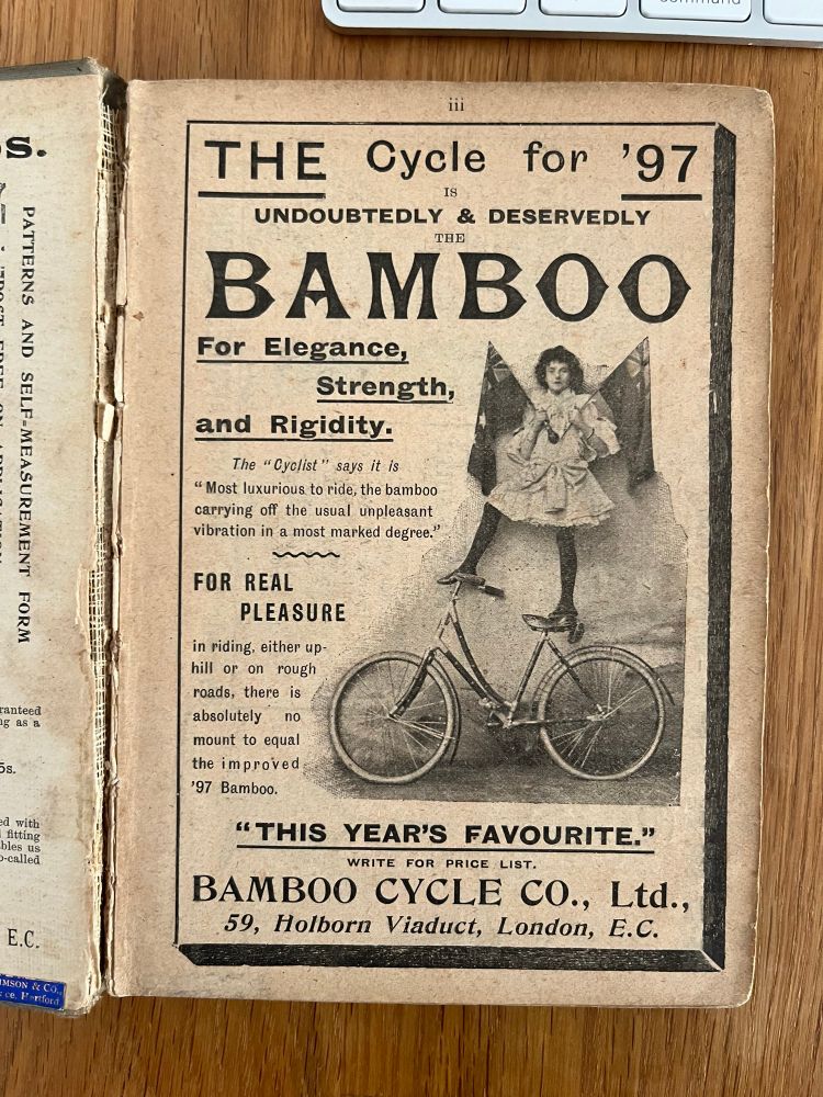 Advert for bamboo bicycles from 1897. “This year’s favourite”. The image is of a young woman balancing on the handlebars and saddle and holding two flags in her hands.