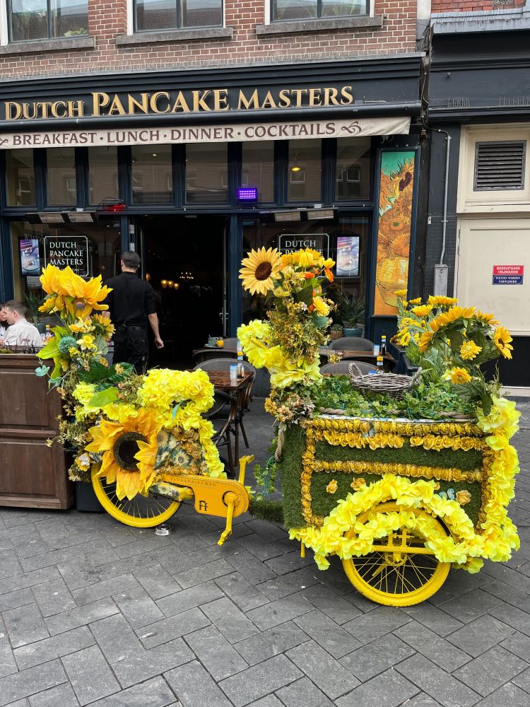 Little yellow cargo bike with yellow wheels, completely decked out in big yellow sunflowers and yellow garlands. Spotted in Amsterdam of course! Behind it is one of Amsterdam's many pancake cafés.