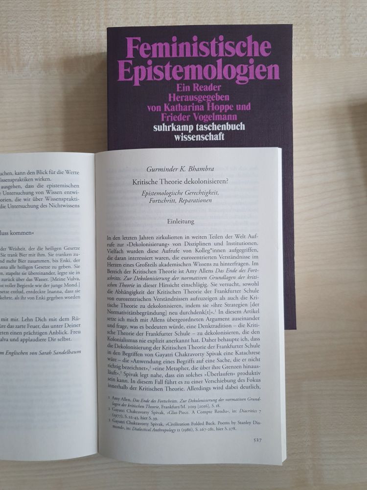 Foto zweier Exemplare des Readers "Feministische Epistemologien" auf einem Schreibtisch. Eines   geschlossen, sodass das Cover sichtbar ist, und eines aufgeschlagen auf der ersten Seite des Beitrags "Kritische Theorie dekolonisieren?" von Gurminder K. Bhambra.