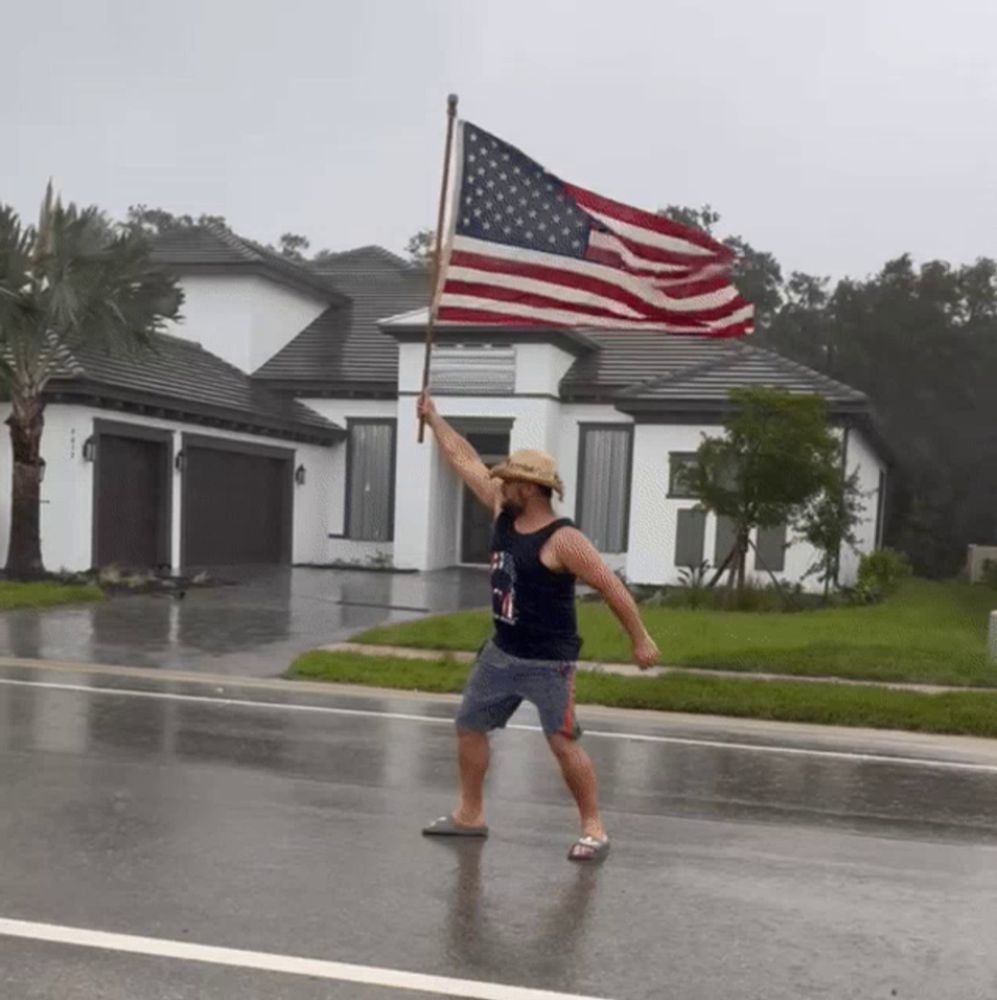 a man in a cowboy hat is holding a large american flag