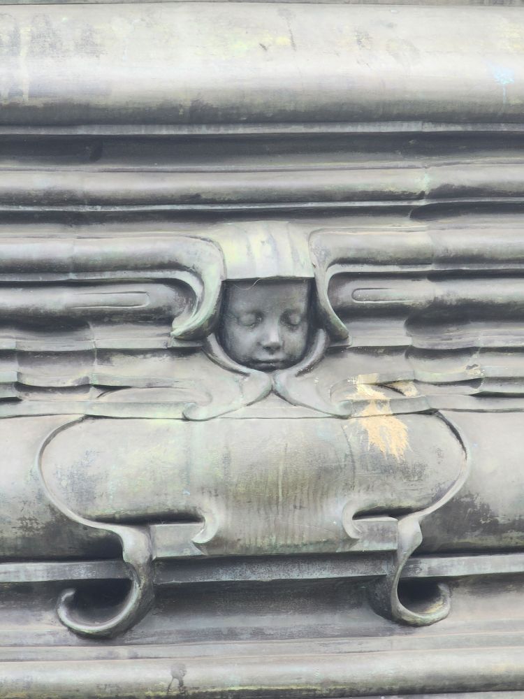 Sleeping cherub(?) below a statue of Queen Victoria 