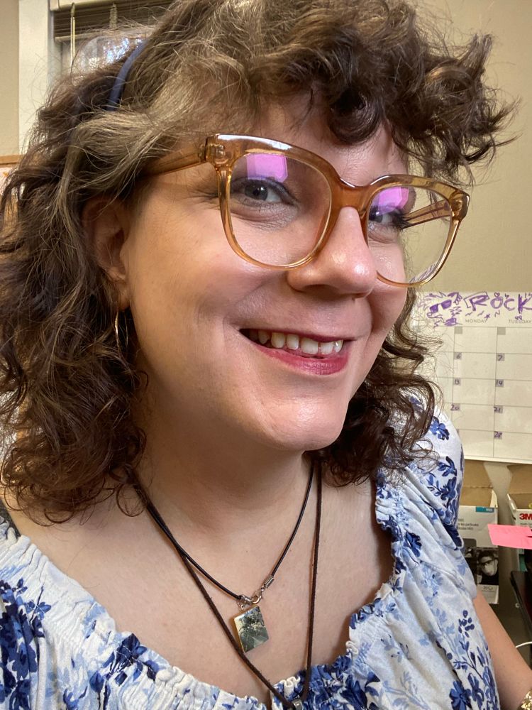 A photo of post transition Molly. She sports a large smile and the same orange glasses from a few years back. 
