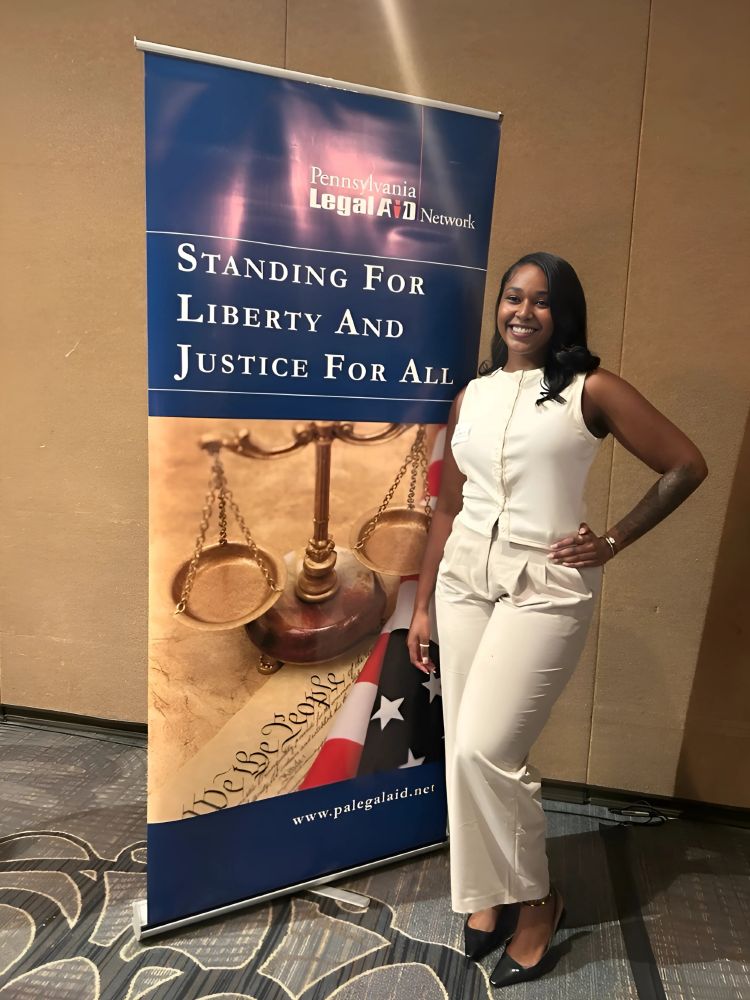 Abbey-Gail Morris, a rising 3L at Widener University Commonwealth Law School, stands beside a Pennsylvania Legal Aid Network banner that reads “Standing for Liberty and Justice for All,” featuring imagery of the scales of justice and the American flag. Morris delivered remarks on behalf of the 2025 MLK, Jr. Summer Internship cohort during the closing reception.