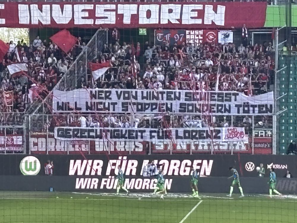 Banner der SC Freiburg Fans:
"Wer von hinten schießt, will nicht stopppen, sondern töten. Gerechtigkeit für Lorenz - Corrillo Ultras"