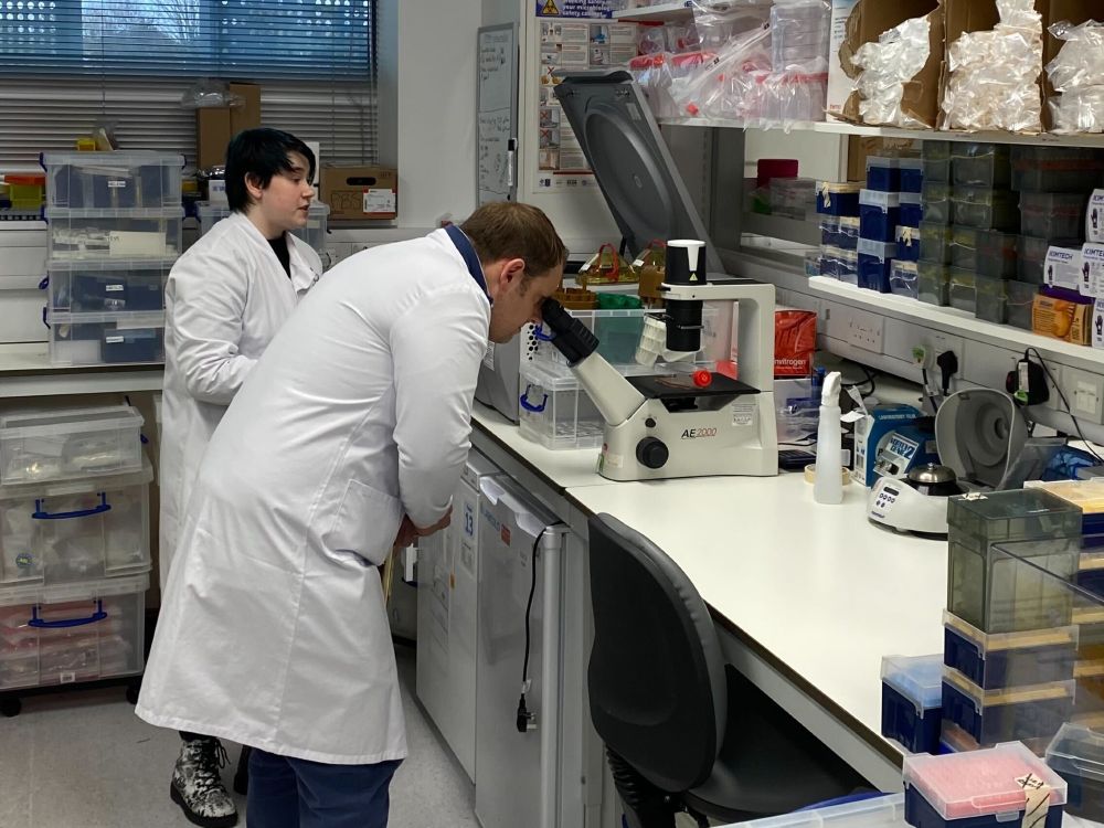 Luke Taylor MP with a cancer researcher. Luke is looking at samples down a microscope.