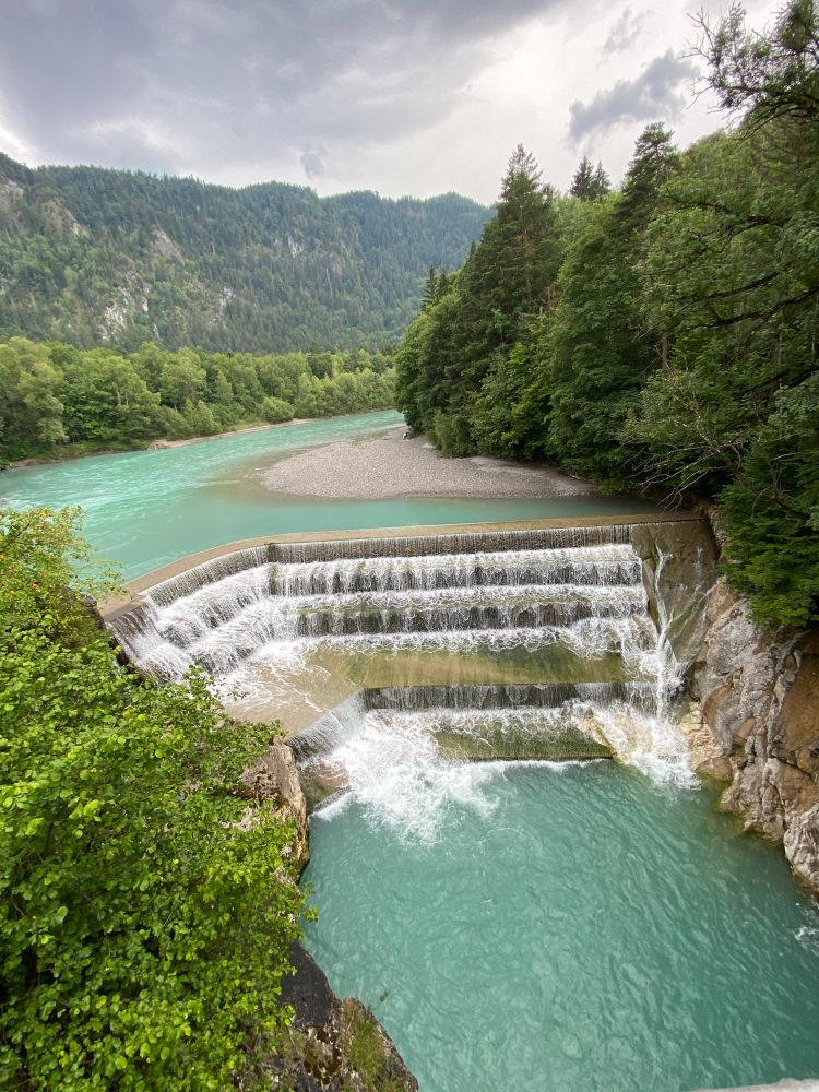 Lechfall in Füssen, türkisfarbenes Wasser, bedeckter Himmel, Bäume, eine Sandbank und der treppenförmige Lechfall