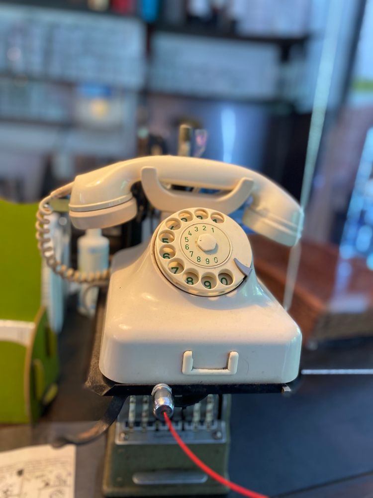 Elfenbeinfarbendes Telefon mit Wählscheibe und rotem Kabel