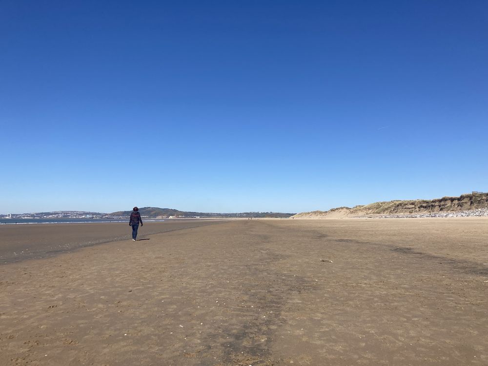 Sandy beach with a single person in the distance walking away. The sky is a deep blue