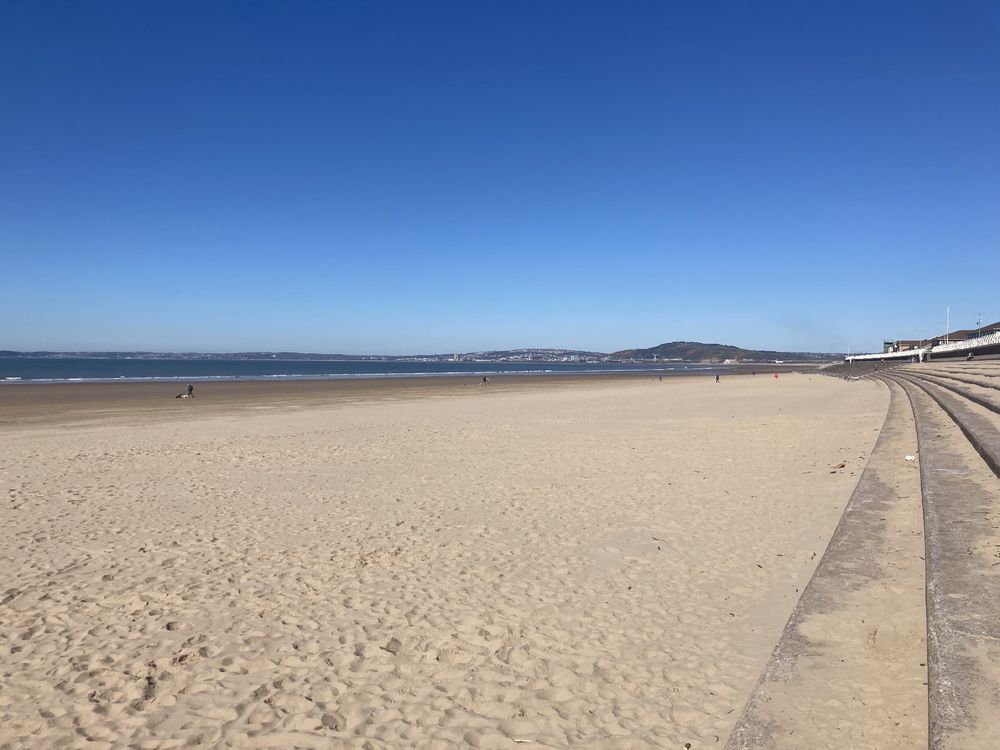 Empty expanse of sandy beach in the foreground with deep blue cloudless sky 