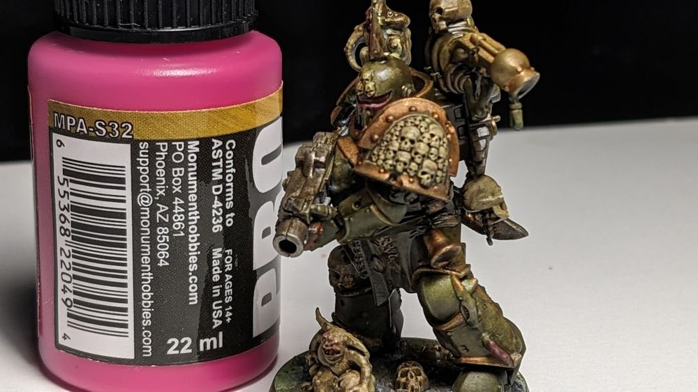 Image is a closeup-shot of a freshly painted Warhammer 40k Death Guard Warrior model standing next to a 22ml bottle of pink paint for scale