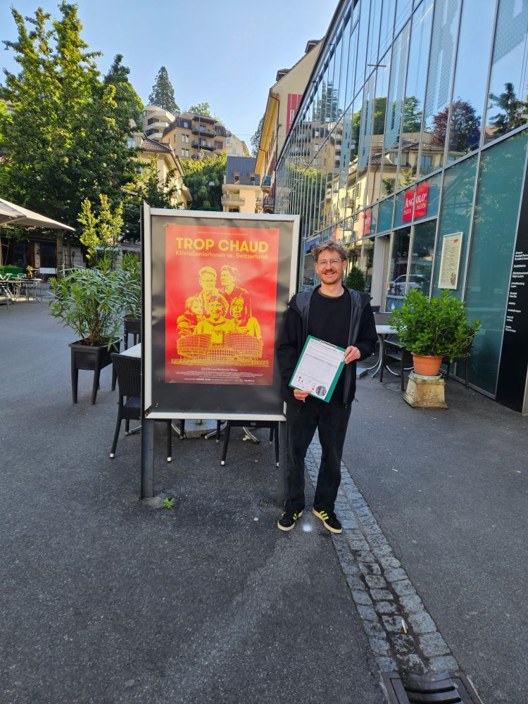 Elias Steiner mit Initiativbogen neben Klimaseniorinnen Plakat