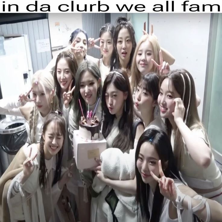 A picture of the kpop girl group LOONA posing around a small cake. The caption above reads "in da clurb we all fam"