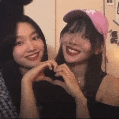 two girls are making a heart shape with their hands while wearing hats .