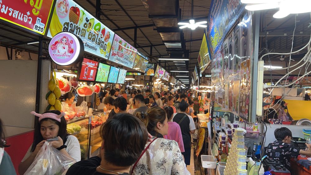 A crowded aisle down the night market. This aisle is full of food stalls. Bright lights coming from every corner of the market make it bright as day. 