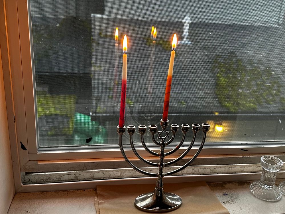 A menorah in the window sill, with a red candle and an orange shamash candle lit.