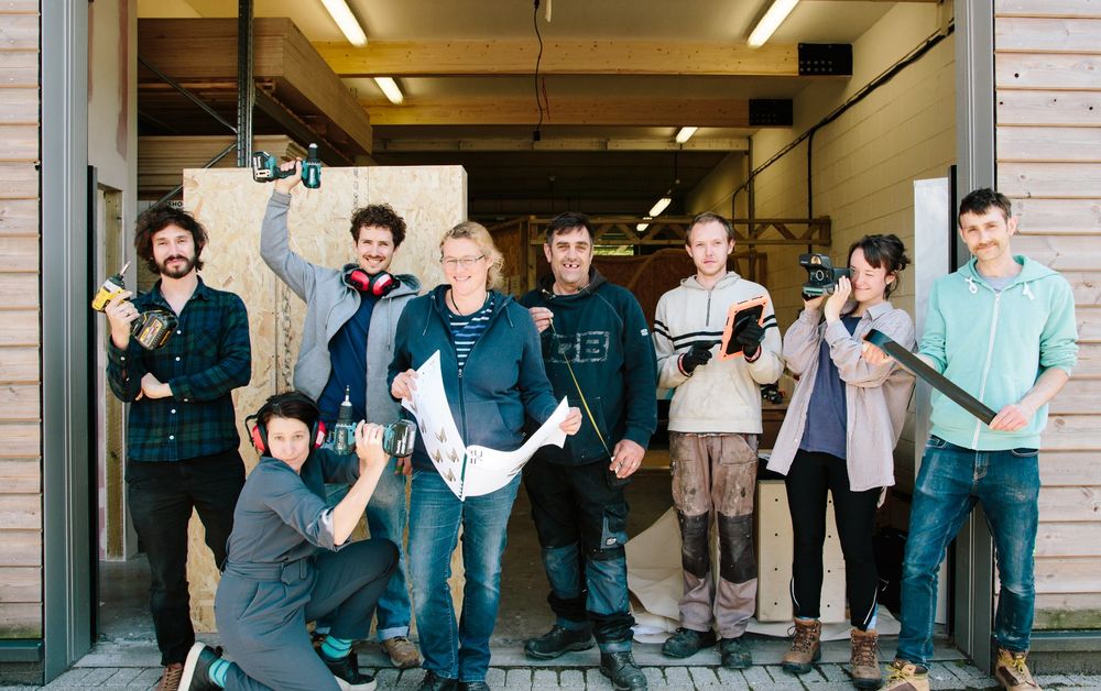 Image of people standing outside a community factory, smiling and brandishing tools.