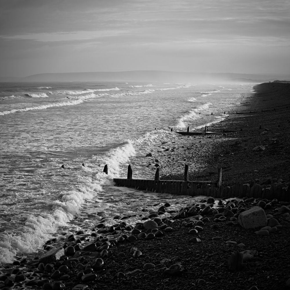 Black and white image of a pebble beach with groynes 