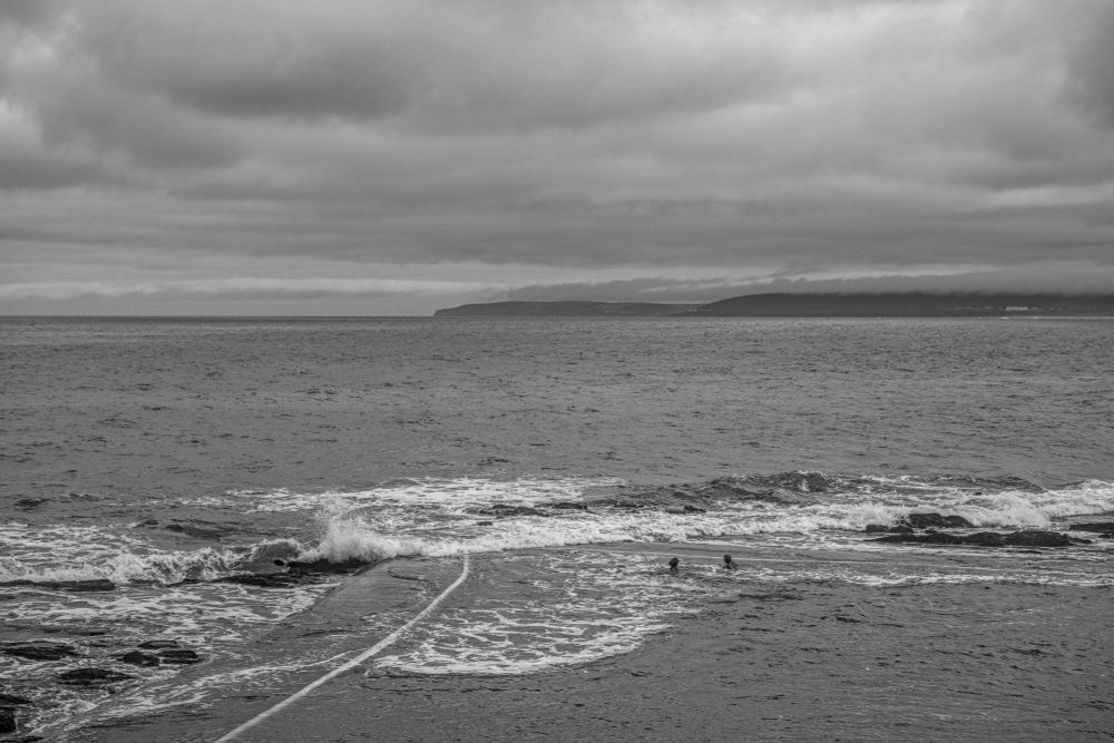 Two people swimming in a victorian rock pool with waves crashing about them