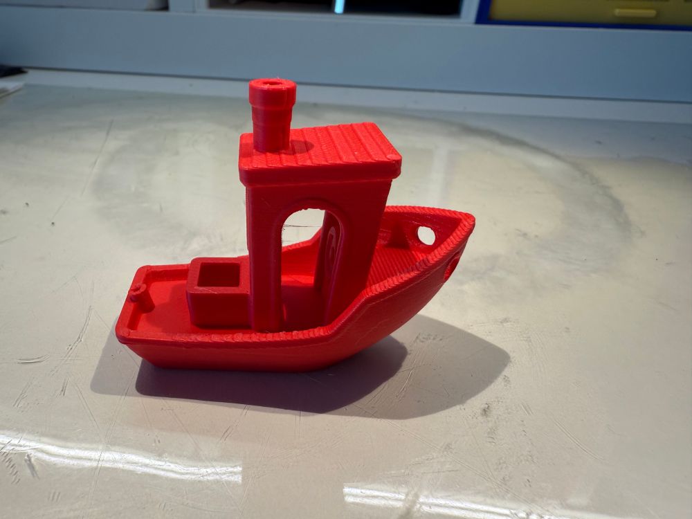 A small red boat. 3D printed typically printed to calibrate a printer. Called a Benchy 
