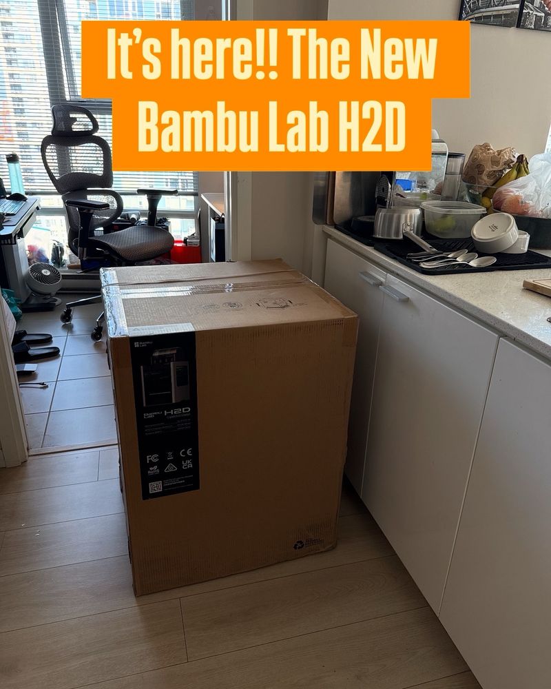 A large box in a kitchen. The box has a label for a 3D printer 