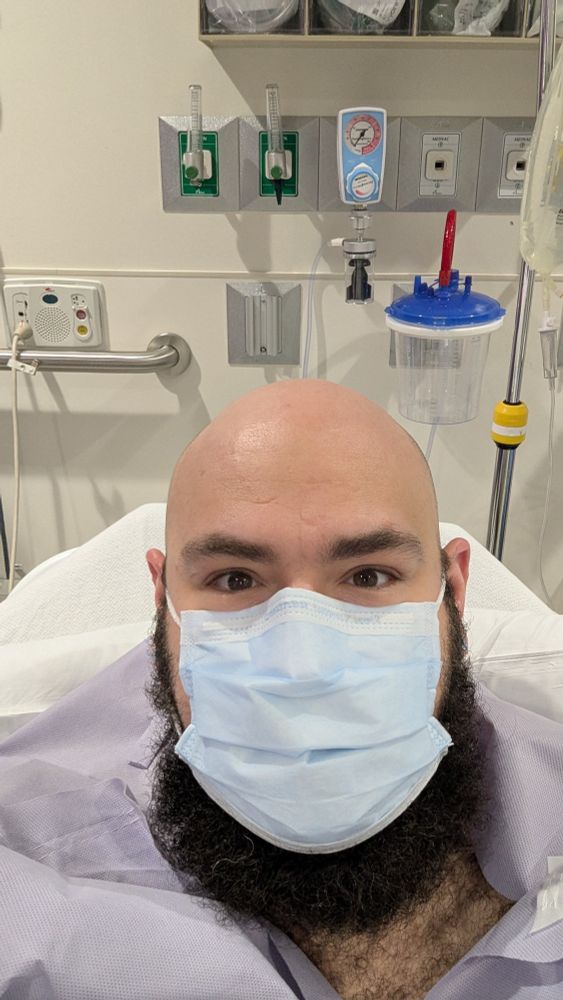 Pre-surgery picture. I'm wearing a face mask and a surgical gown. In the background there are many hospital things because I'm in a hospital.