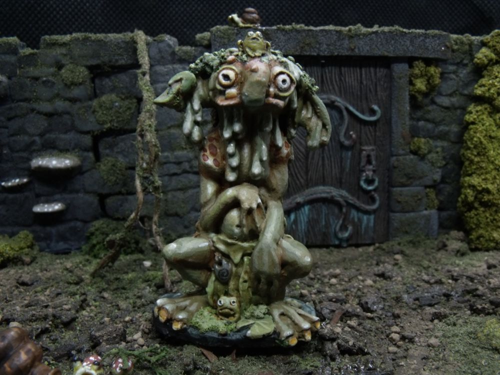 a photo of a miniature troll with a frog on his head, there are walls and moss in the background and scattered snails and mushrooms
