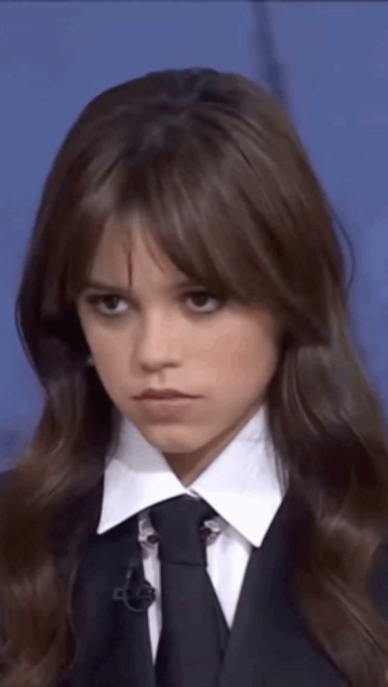 a young girl wearing a suit and tie looks at the camera with a serious look on her face