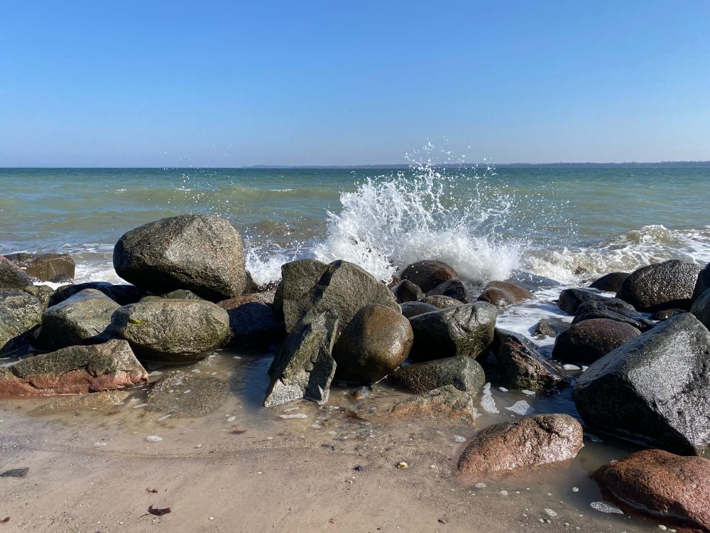 Blauer Himmel, Wellenbrechersteine, Meer mit Gischt