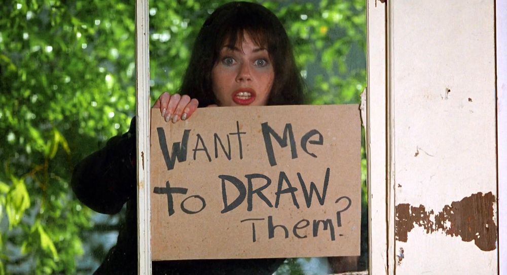 an edit of Fairuza Balk's character in Waterboy, holding up a cardboard sign with marker writing on it. it has been altered to say "want me to draw them?"