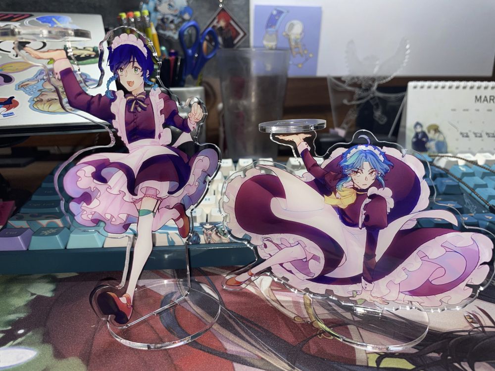 Two acrylic standees of Venti and Xiao from Genshin Impact dressed as maids. They both have small acrylic "plates" that can be used to hold objects.