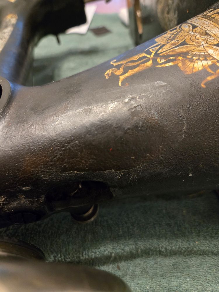 A section of an antique sewing machine, just behind the hand wheel, showing a definitive line in a vaguely oval shape. Visible on either side is caked on grease and dust and who knows what else