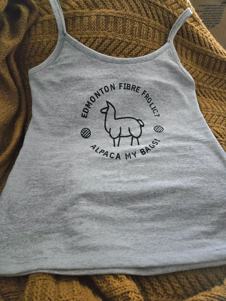 A grey top with thin straps lays against a knit blanket. It reads "Edmonton Fibre Frolic" and "Alpaca My Bags!" with a stylized alpaca between them.