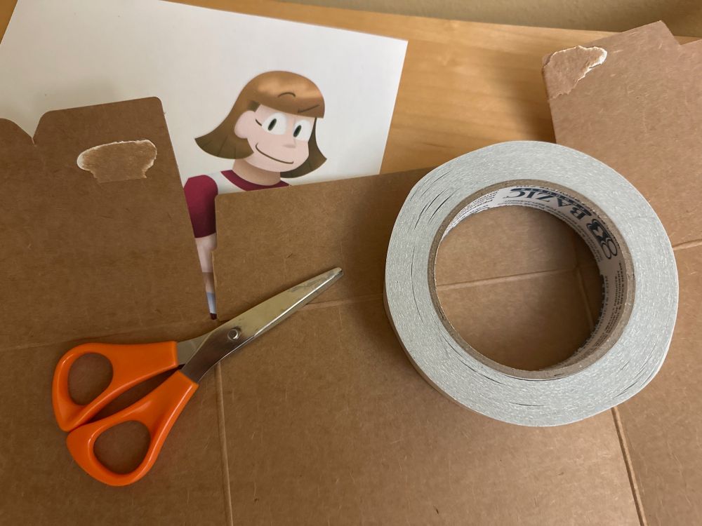 A photo of the material I used splayed out on a table; a sheet of paper with the picture of the girl printed out, a pair of scissors, a roll of double-sided tape, and cardboard from a disassembled Cinnamon Toast Crunch cereal box.