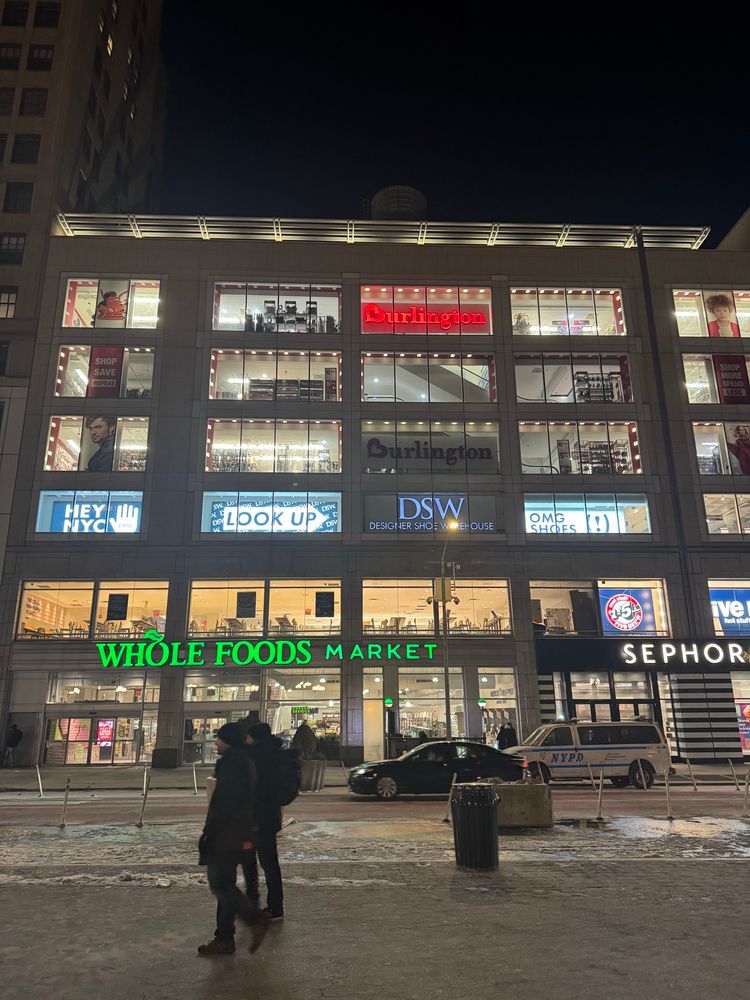 A building with many windows facing Union square, taken from across the street. The building has a DSW store on the second floor with an advertisement that says “Hey NYC, LOOK UP > OMG SHOES (!)”