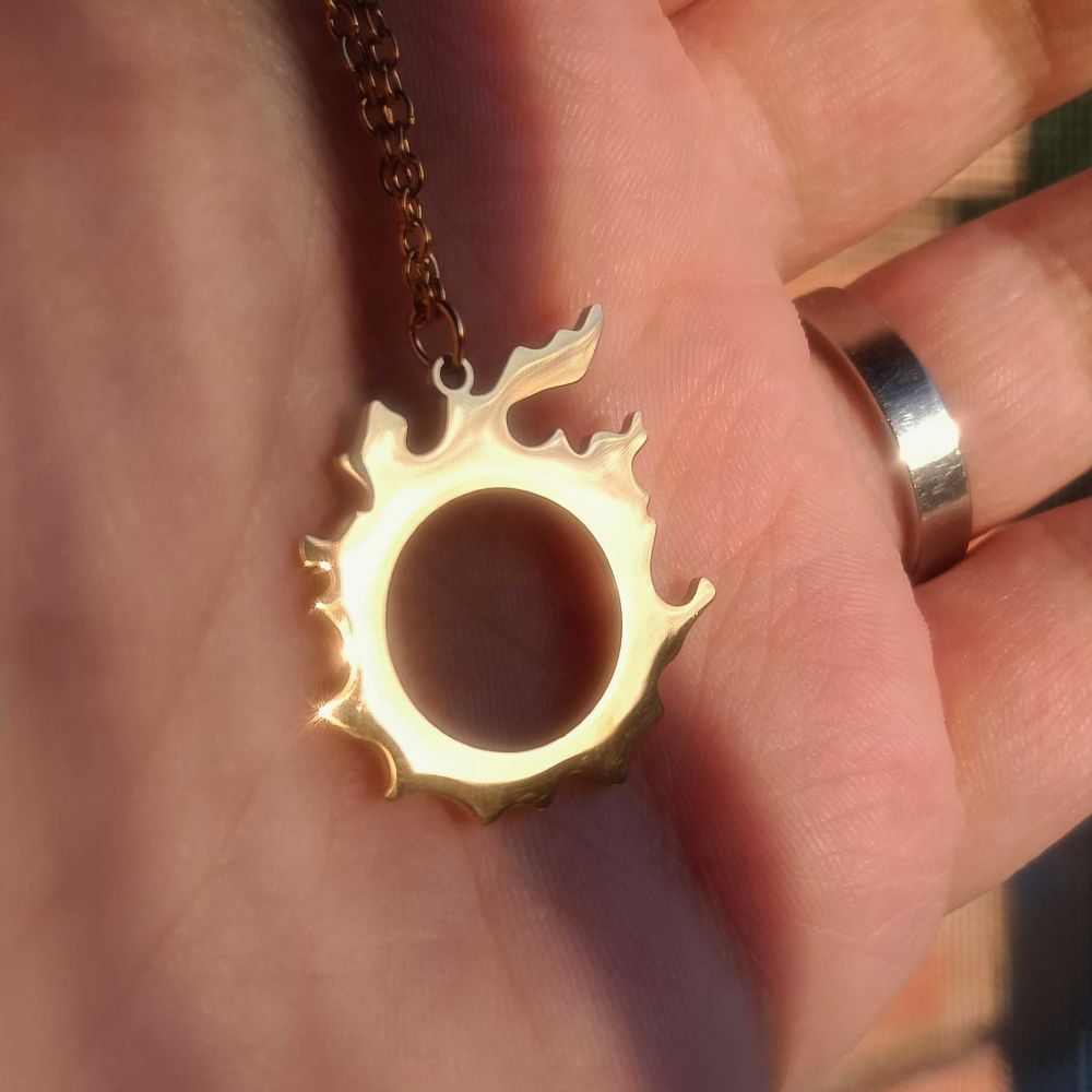 A hand holding a golden necklace with the Meteor Symbol from the MMO Final Fantasy XIV