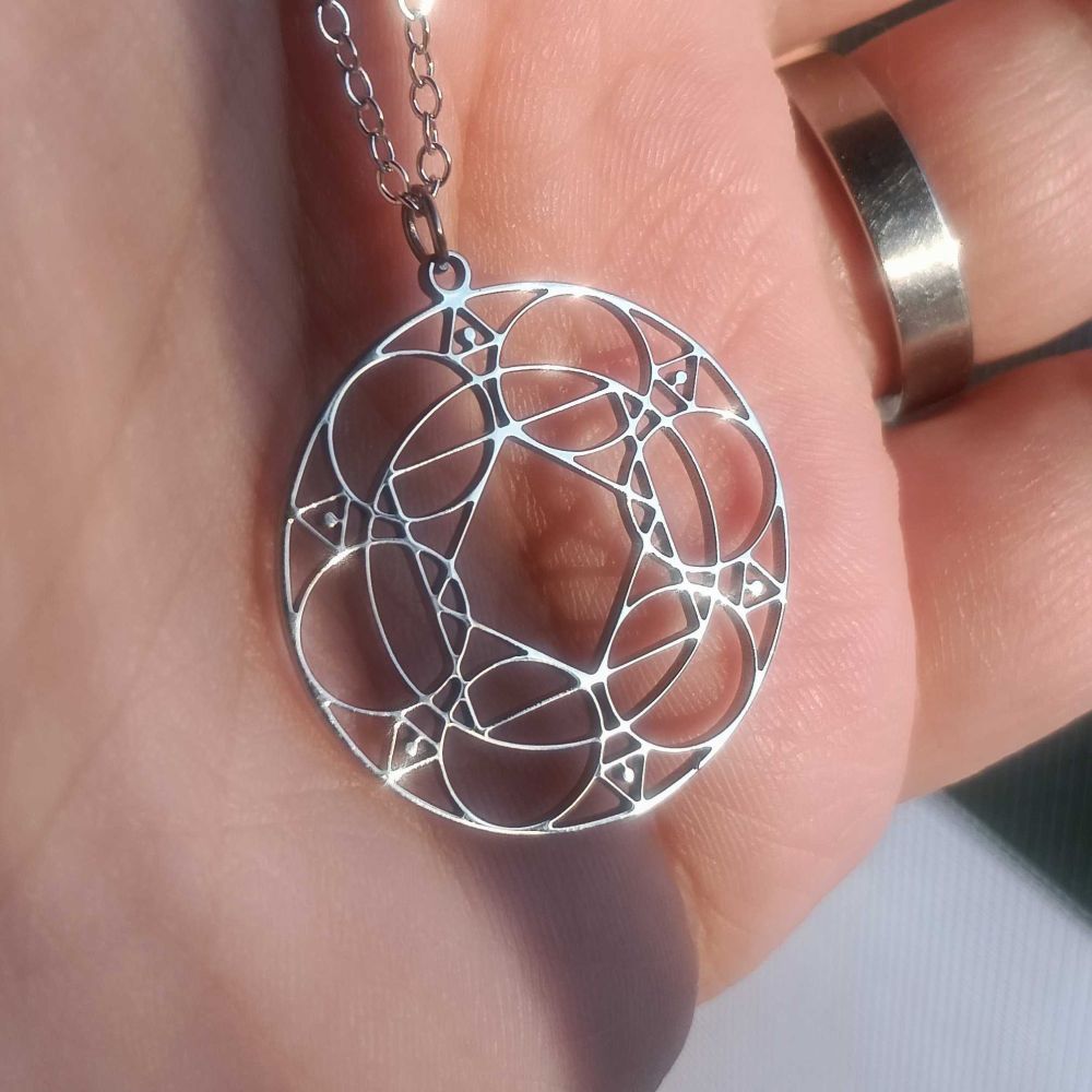 A hand holding a charm necklace that has a Black Mage's Ley Lines as a design, from the same ability used by black mages from the MMO Final Fantasy XIV