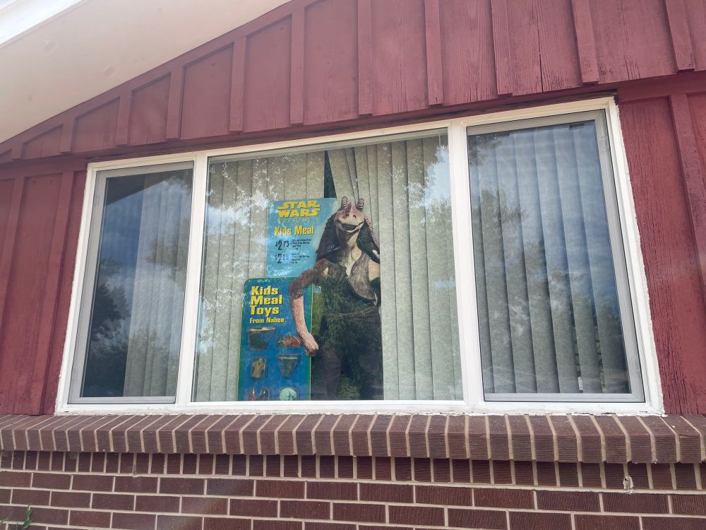 Photo of a house with a 1999 Star Wars Episode I: The Phantom Menace KFC promotional standee of Jar Jar Binks in the front window 