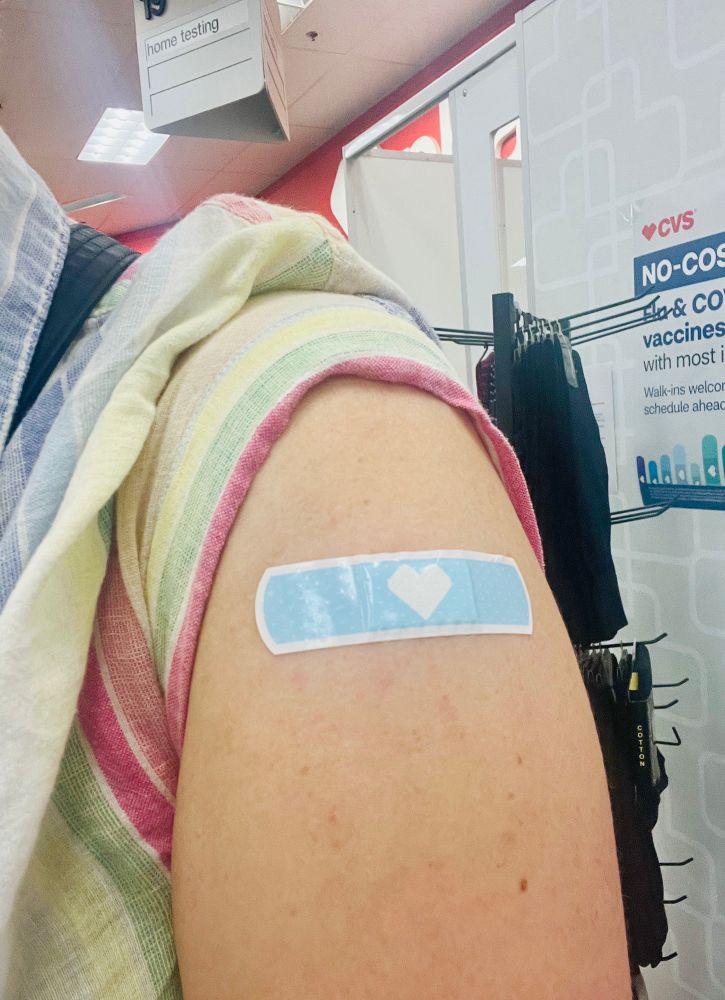 Emily’s arm with her sleeve rolled up, shoving a blue CVS bandaid with a heart where she was vaccinated. 