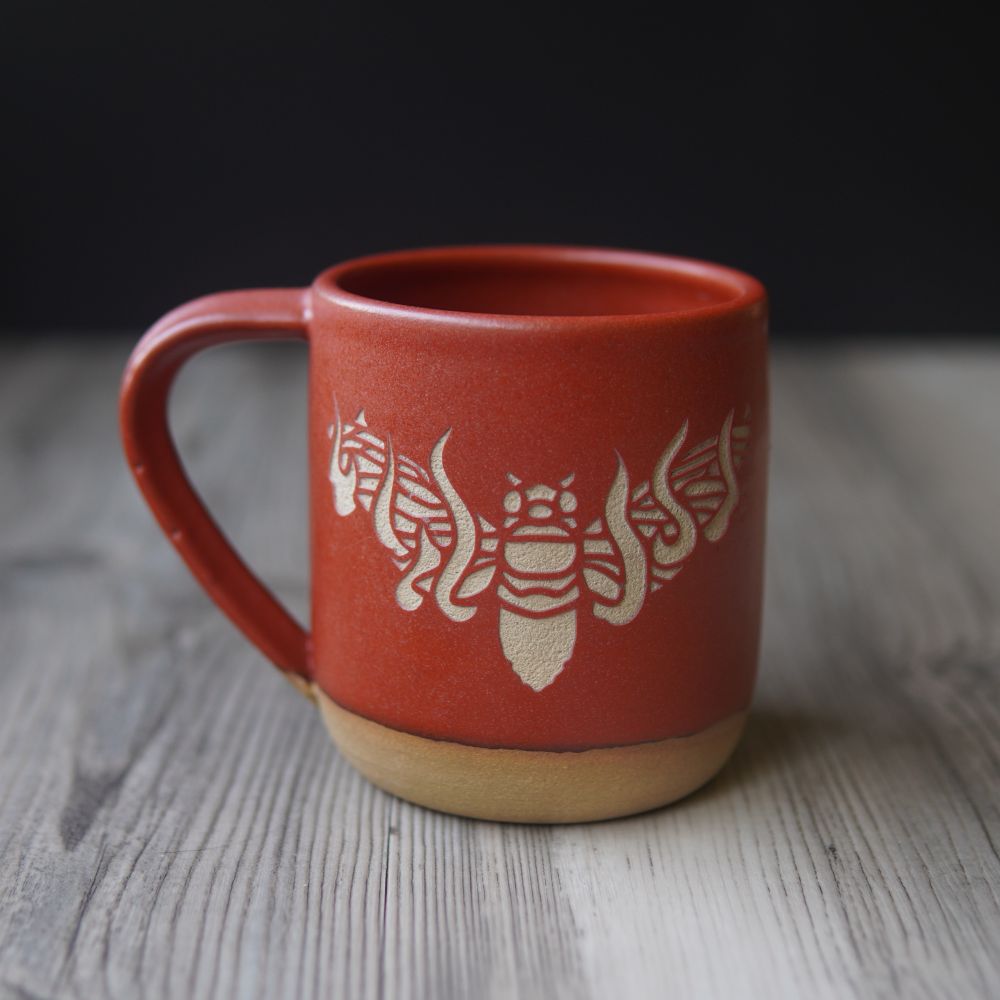 An orangey-red mug engraved with a flaming cicada