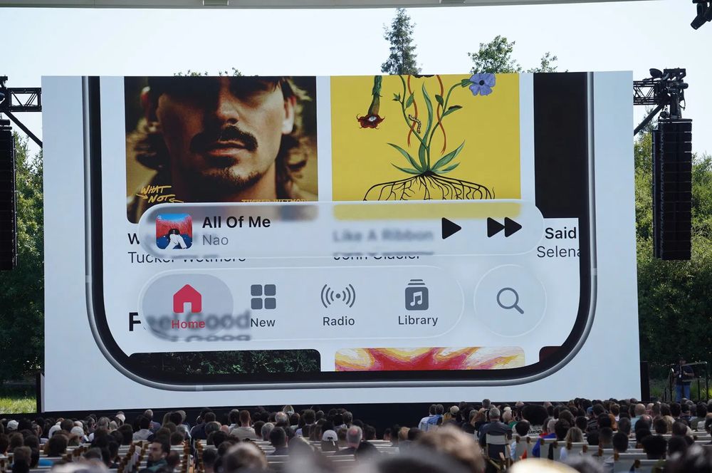 Photo from WWDC showing Apple's new "Liquid Glass" in Apple Music. The albums and text on display are visible right through the player controls and buttons for "Home", "Library", etc making legibility very difficult