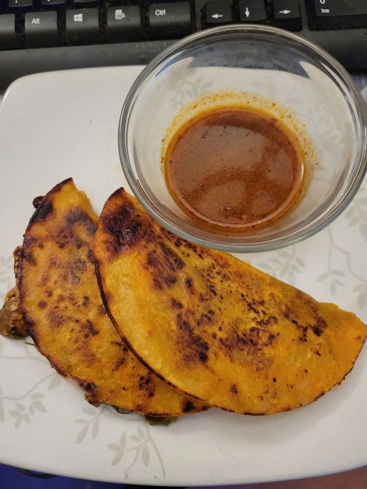 A small plate of birria tacos, made with tofu and mushrooms, corn tortillas, dipped and fried in a pan, with white cheese, and a side of birria sauce for dipping.