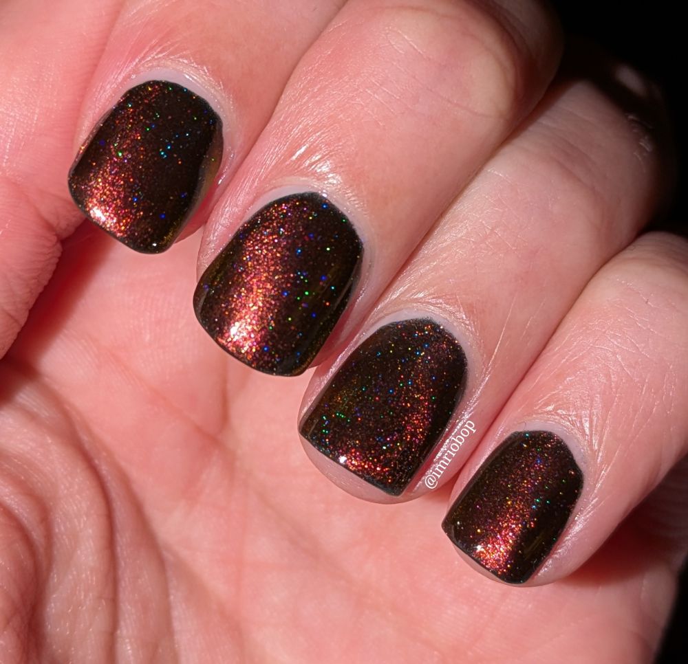 Flash photo of Starrily "Wake Up. This is a magnetic nail polish set in the velvet style design which brings the magnetic pigment to the surface of the nail which will cause color shifts to happen depending on the angle. This angle highlights the warm red shift along with rainbow holographic glitter across the nails.