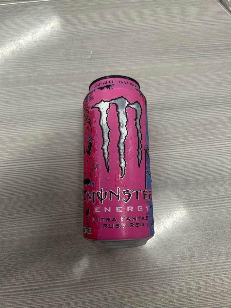 a monster energy drink sitting on the desk.
the black text on the bottom reading: "ultra fantasy ruby red"