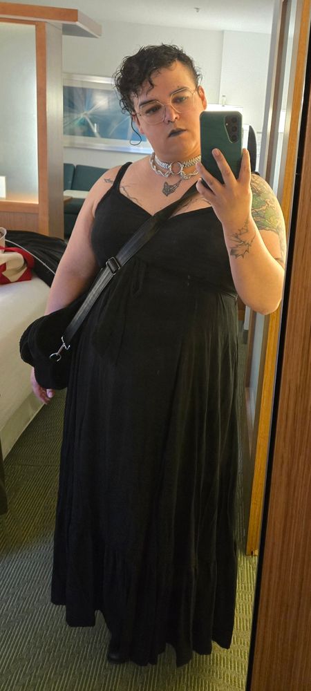 Mila posing in a hotel mirror. She's wearing a full length black dress with a chain mail necklace. Her hair is pinned up.