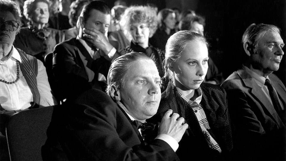 Ein Film-Still aus Aki Kaurismäkis "Hamlet goes business"
Hamlet sitzt in einem Smoking im Theater, blickt verängstigt auf die Bühne, ist etwas in den Sitz versunken und lehnt sich leicht an Ophelia an, die neben ihm sitzt 